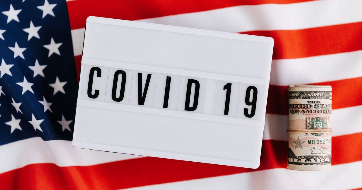 From above of plastic signboard with COVID 19 inscription on flag of USA and roll of paper money during financial crisis