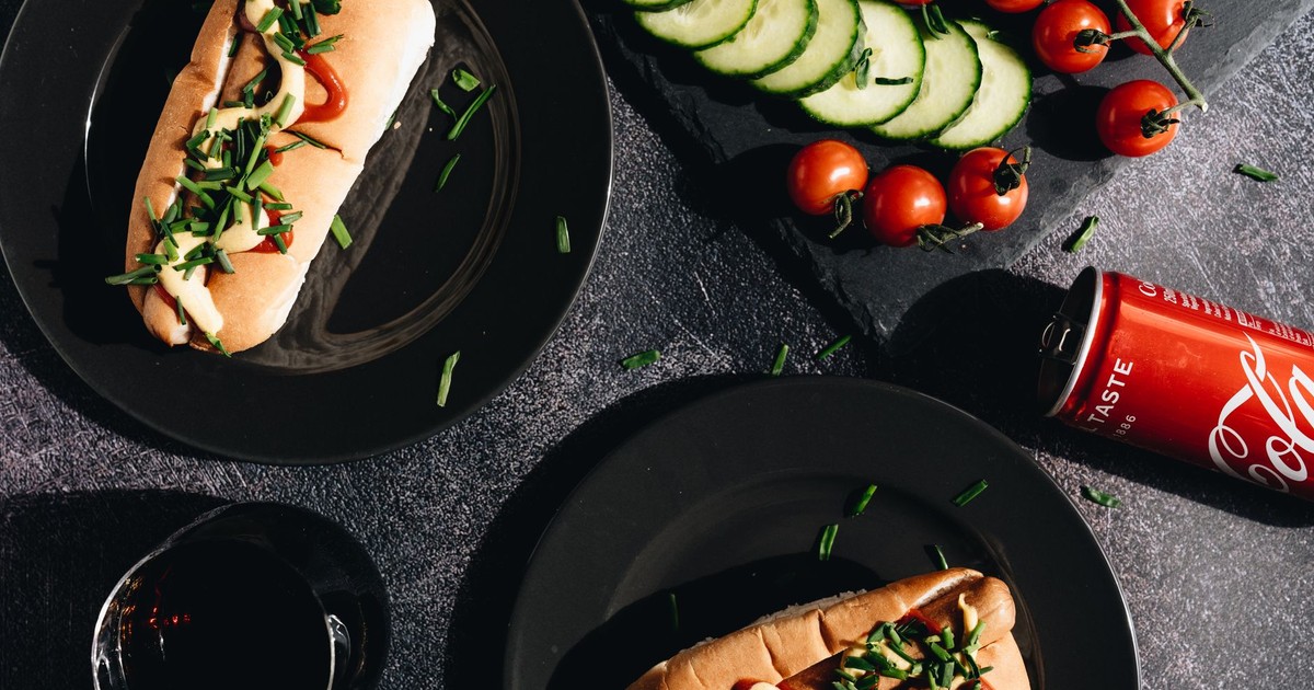 Savor gourmet hot dogs topped with fresh vegetables, served with a refreshing cola.