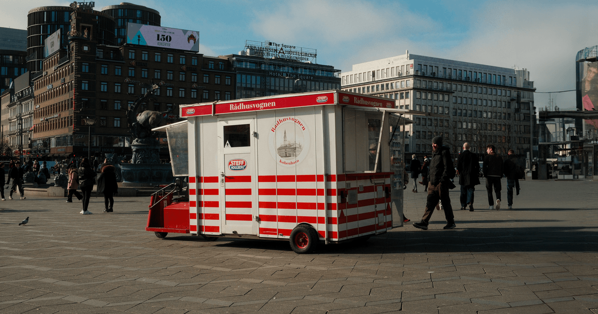 Street hot dog cart in a bustling city square with modern buildings around.