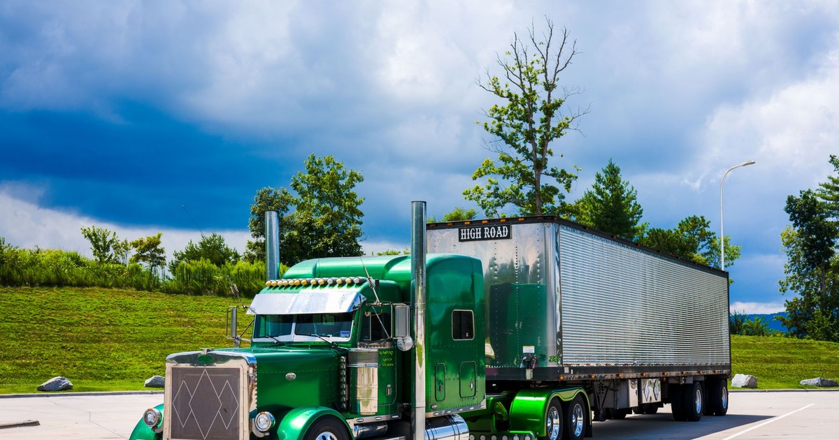 A striking green semi-truck parked outdoors with a dramatic cloudy sky backdrop.