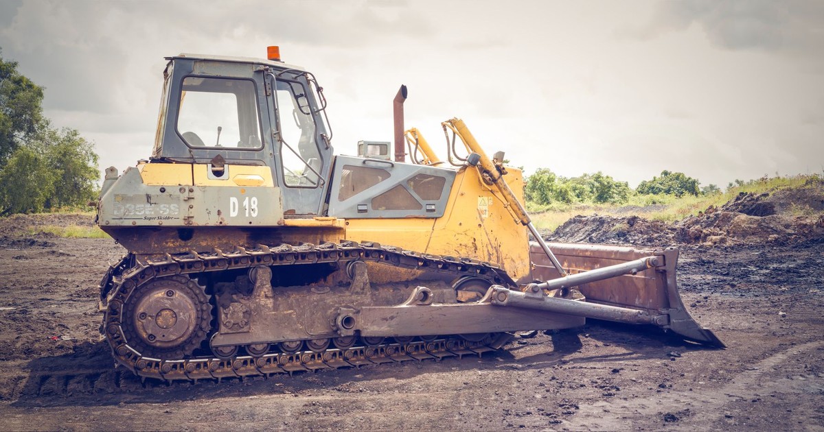 A powerful bulldozer on muddy construction ground under a cloudy sky.