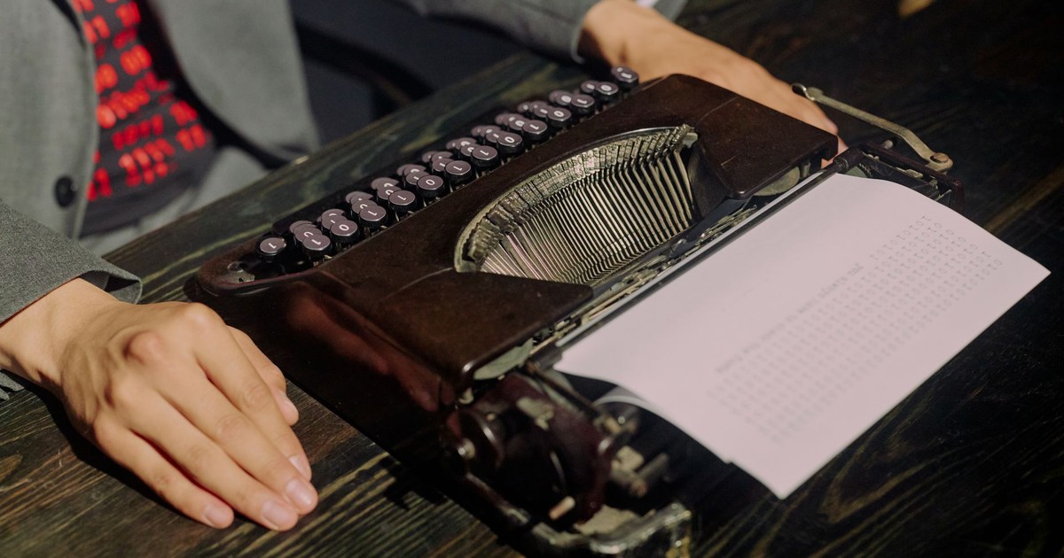 A person uses a vintage typewriter to type on paper in a retro office setting.