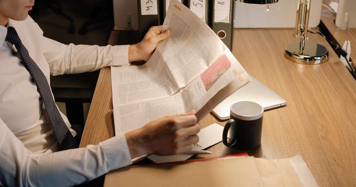 A focused businessman reads a newspaper at a wooden desk in his office, emphasizing work and information.