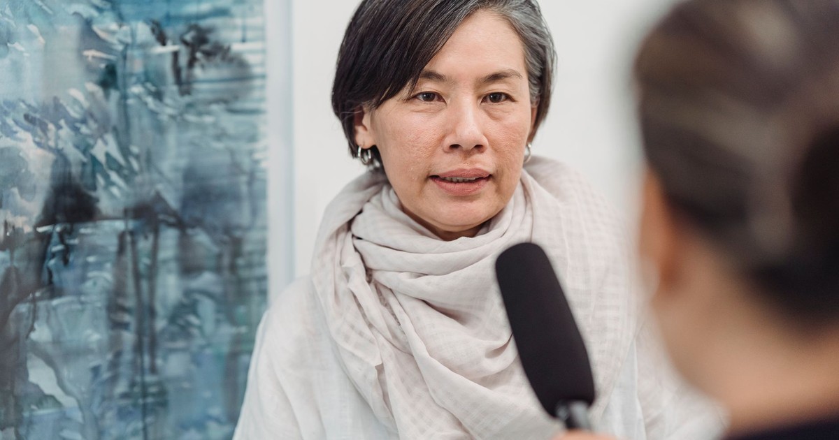 Asian woman in discussion with a journalist at an indoor art gallery.