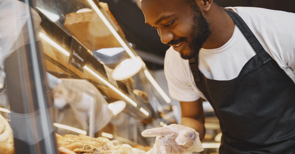A cheerful baker in a bakery showcases fresh pastries behind a glass display case.
