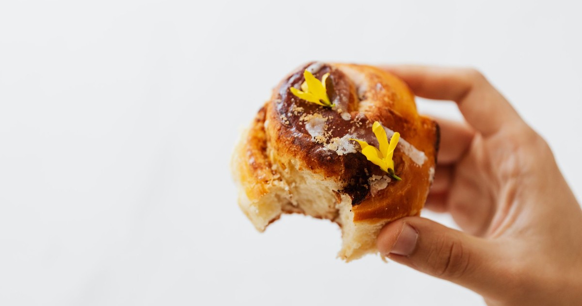 Close-up of a delicious cinnamon roll with a bite missing, held by hand.