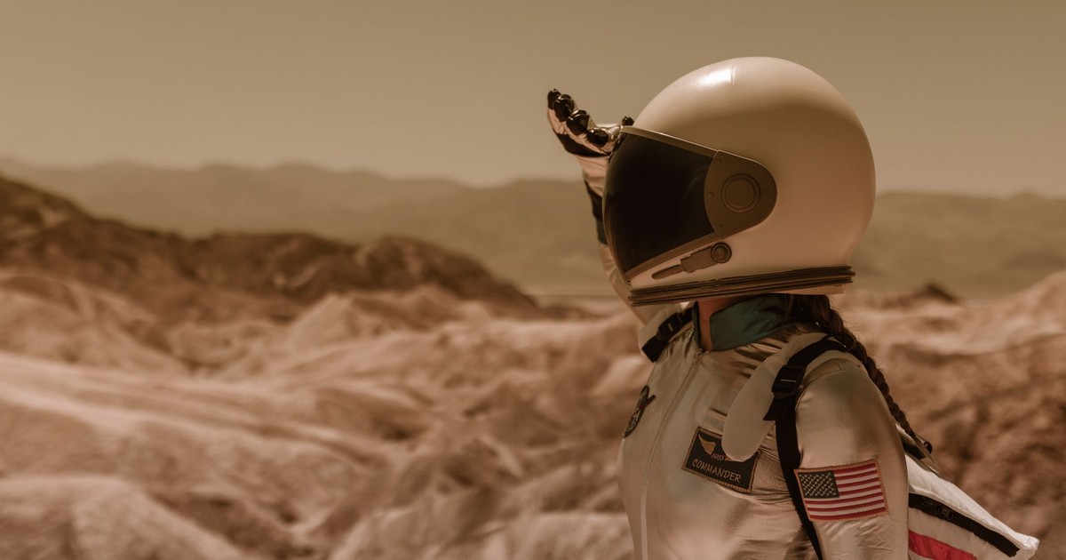 An astronaut in a space suit explores a desolate rocky landscape under a bright sky.
