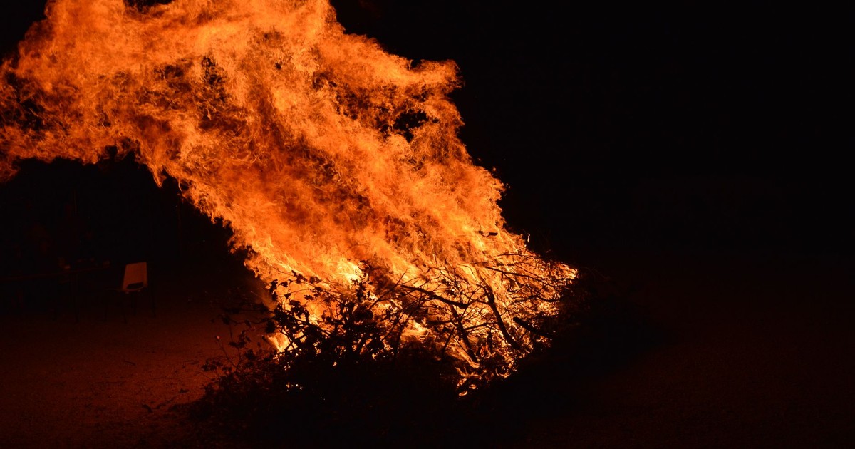 A large bonfire ablaze under the night sky, creating a dramatic fiery scene outdoors.