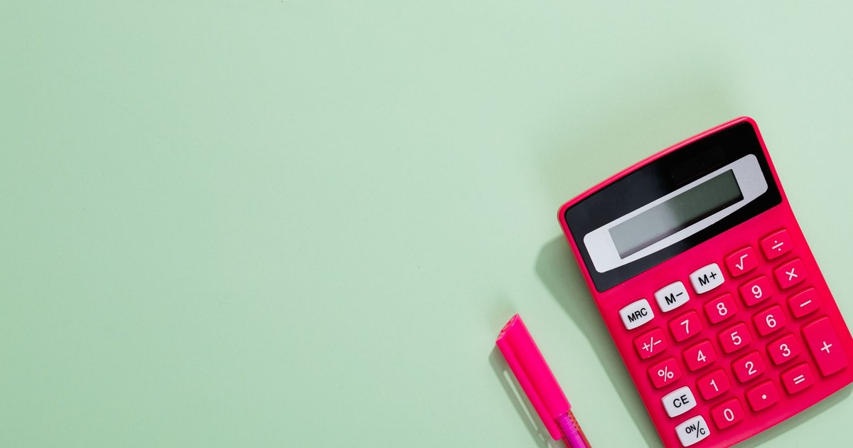 Pink calculator and pen on a pastel green background with copy space.