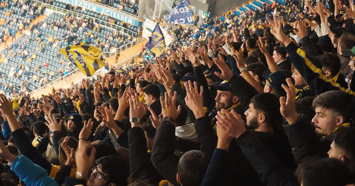 Energetic fans with raised hands in a stadium, supporting their soccer team with enthusiasm.