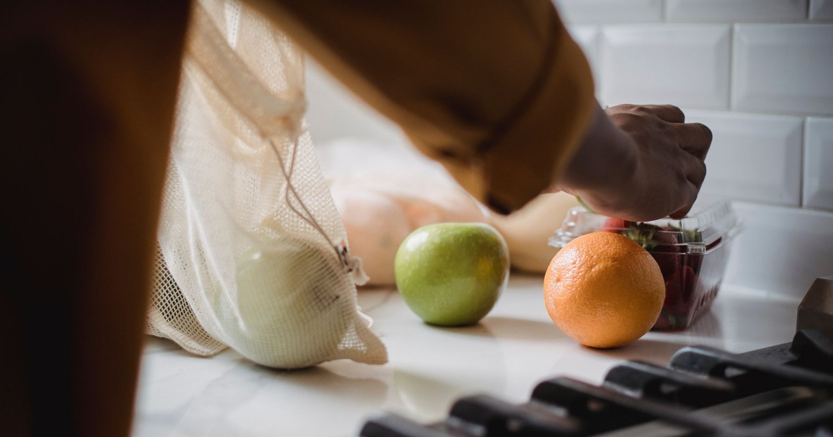 Person unpacking eco-friendly bag with fresh fruits in a modern kitchen.
