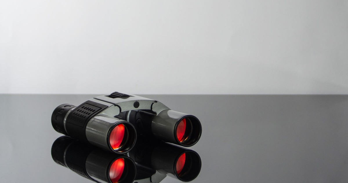 Close-up of modern binoculars with red lenses reflecting on a sleek glass surface.