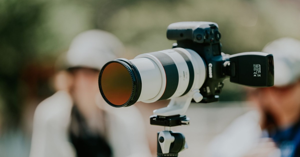 Professional camera with telephoto lens on tripod, blurred outdoor background, showing focus and precision.