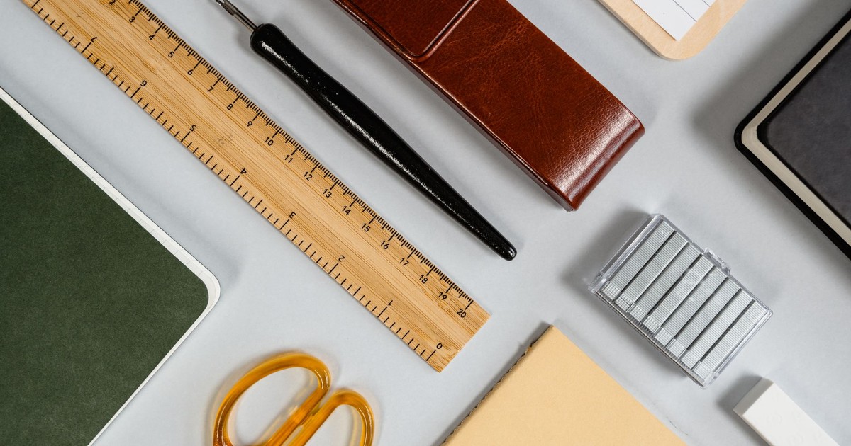 A variety of stationery including scissors, ruler, and notebook arranged in an organized flat lay on a desk.
