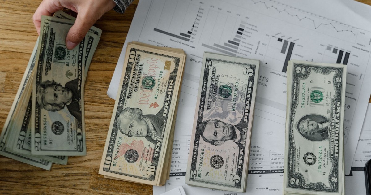 Person holds US dollars over financial papers, showing income or budget analysis.