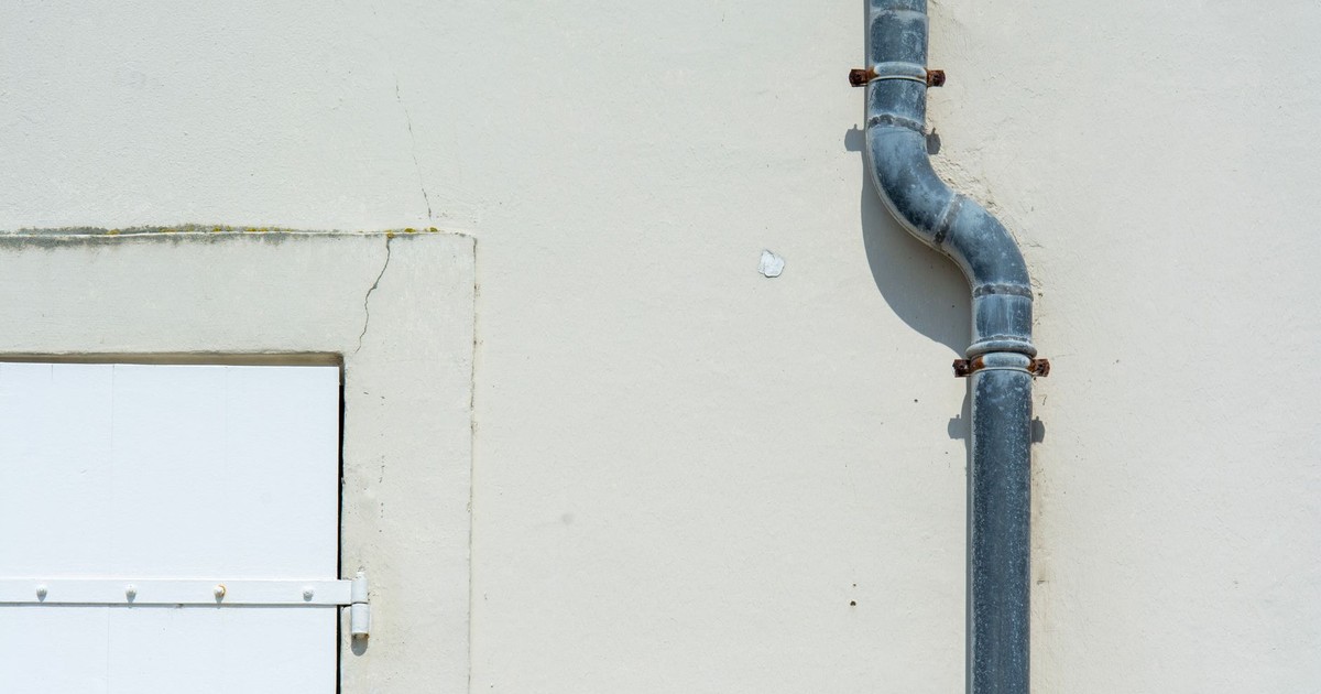 Close-up of a gray metal drainpipe attached to a plain exterior wall.