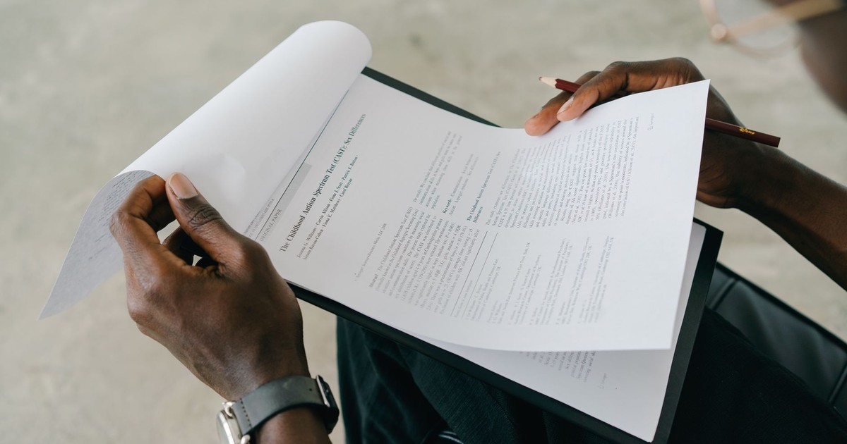 Hands holding and reviewing business documents with a pen, focusing on detailed paperwork.