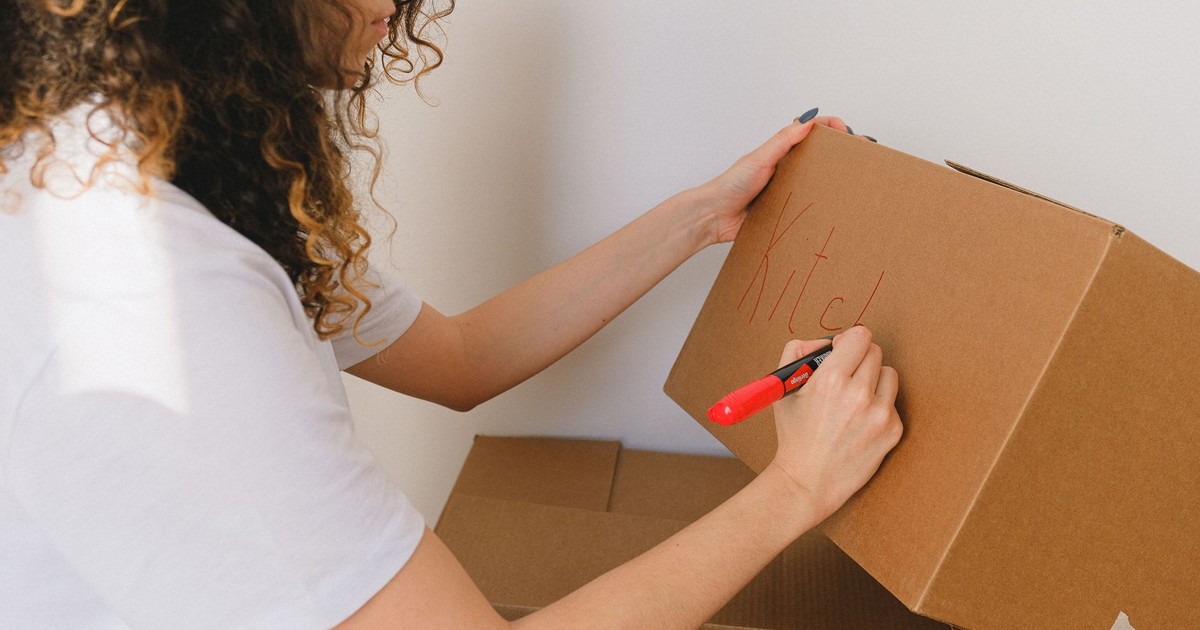Woman organizing and labeling cardboard boxes for moving indoors.