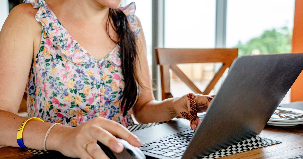 A woman using a laptop for remote work indoors, featuring a floral dress and henna design.