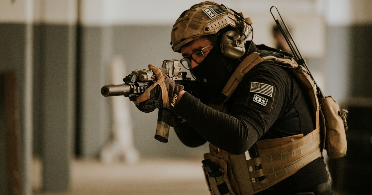 A soldier in tactical gear aims a rifle during indoor military training.