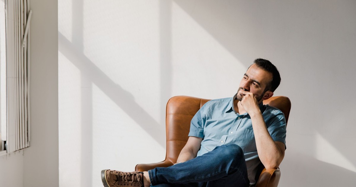 Man in casual attire sitting thoughtfully in a sunlit room, deep in contemplation.
