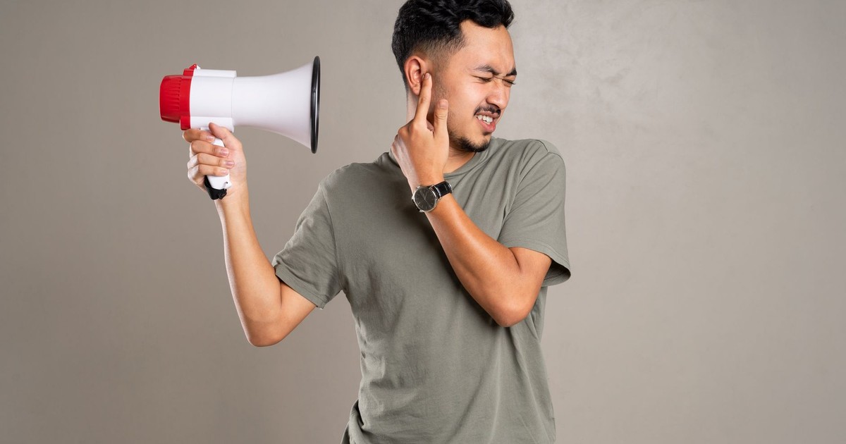 A man with a megaphone holding ear in discomfort, representing noise pollution or loud sounds.