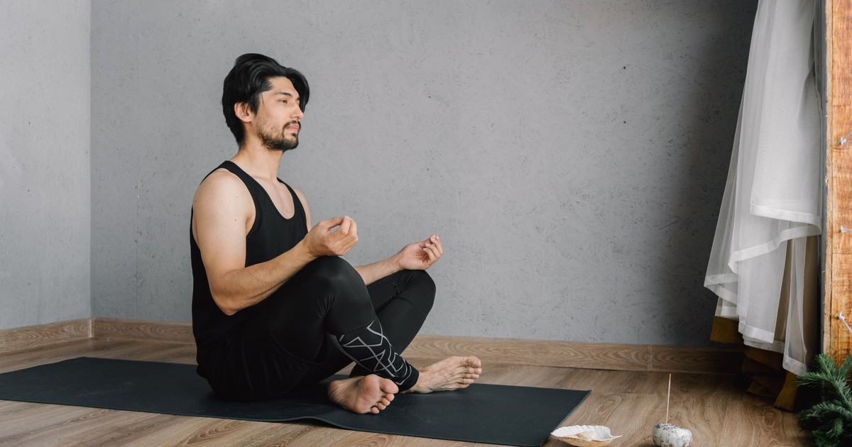 Asian man practicing meditation indoors on a yoga mat, focusing on well-being and mindfulness.