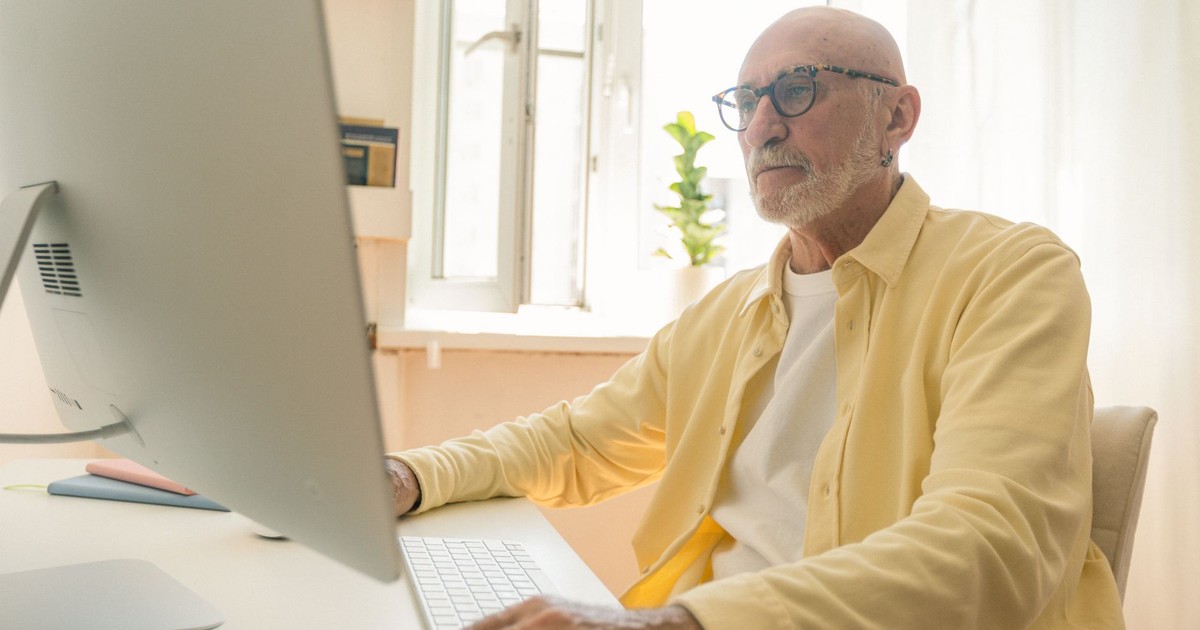 Elderly man with eyeglasses working attentively on a desktop computer indoors.