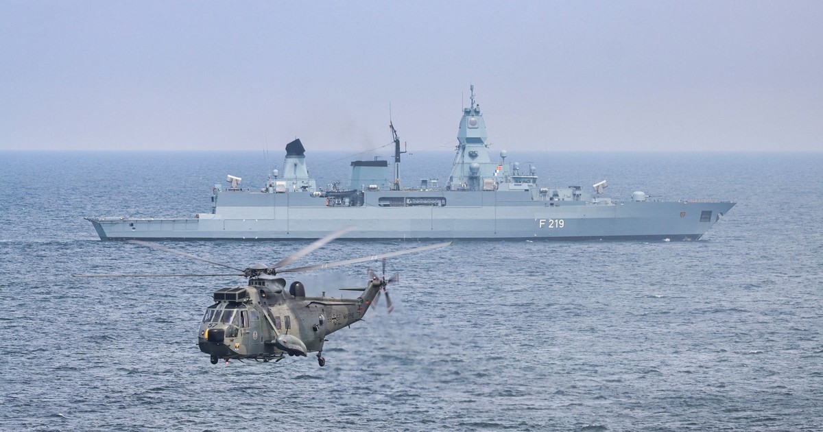 A military helicopter flies over the sea near a German warship, F219.