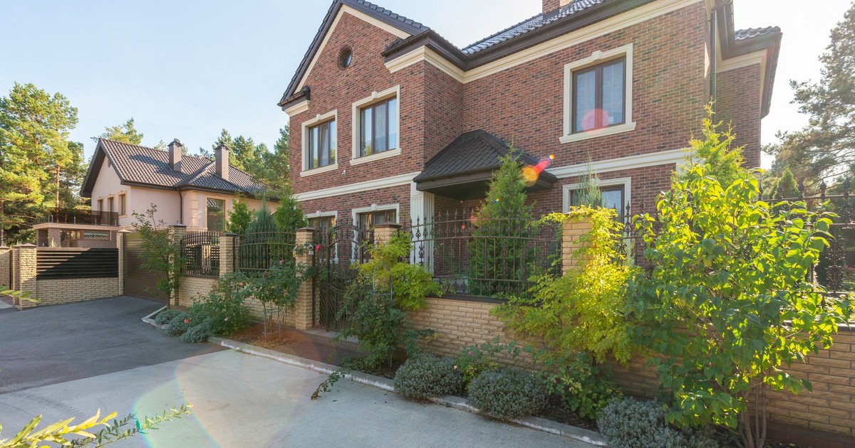 Elegant brick house with a lush garden and driveway, under a clear sky.