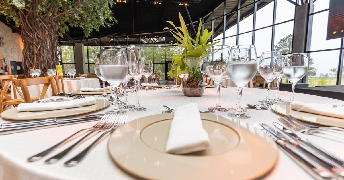 Elegant table setup with glassware, plates, and greenery in a modern restaurant setting.