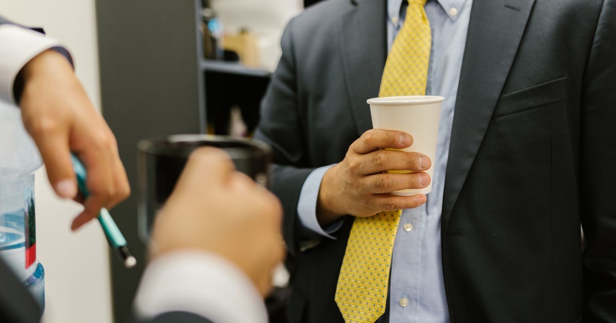 Close-up of business professionals networking, holding paper cups in office attire.