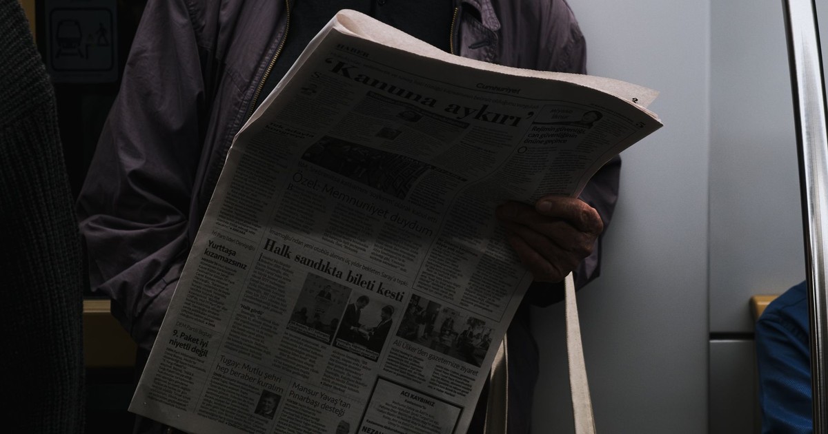 A man reads a newspaper in a dimly lit public transport setting, reflecting city life.