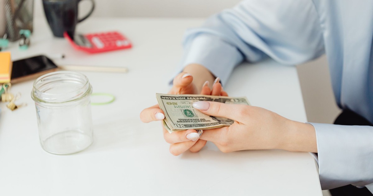 Close-up of hands counting US dollar bills on a white desk with office supplies.