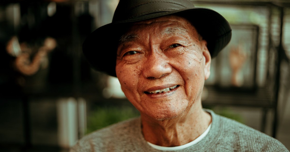 Warm portrait of a smiling elderly man wearing a hat, indoors with soft lighting.