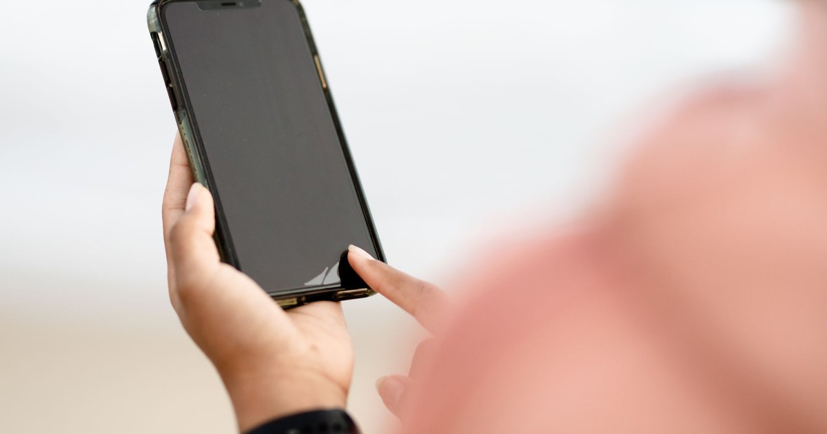 A hand interacting with a smartphone touchscreen outdoors. Modern technology concept.