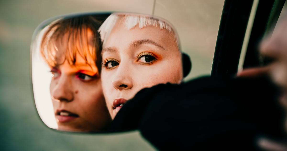 Stylish portrait of two women looking into a car mirror, capturing an intimate and artistic reflection.