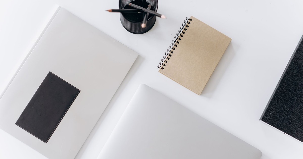 Top view of modern laptop with notebooks and cup of pencils composed on white table in office