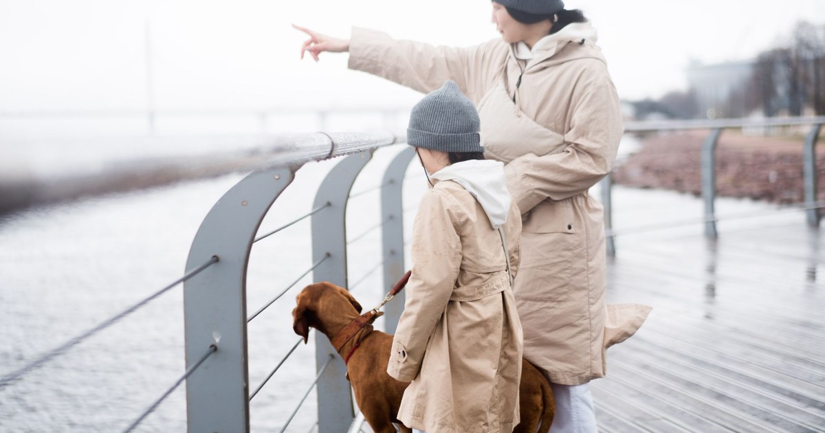 Mother and child in coats walking dog by the seaside, pointing at distant views.