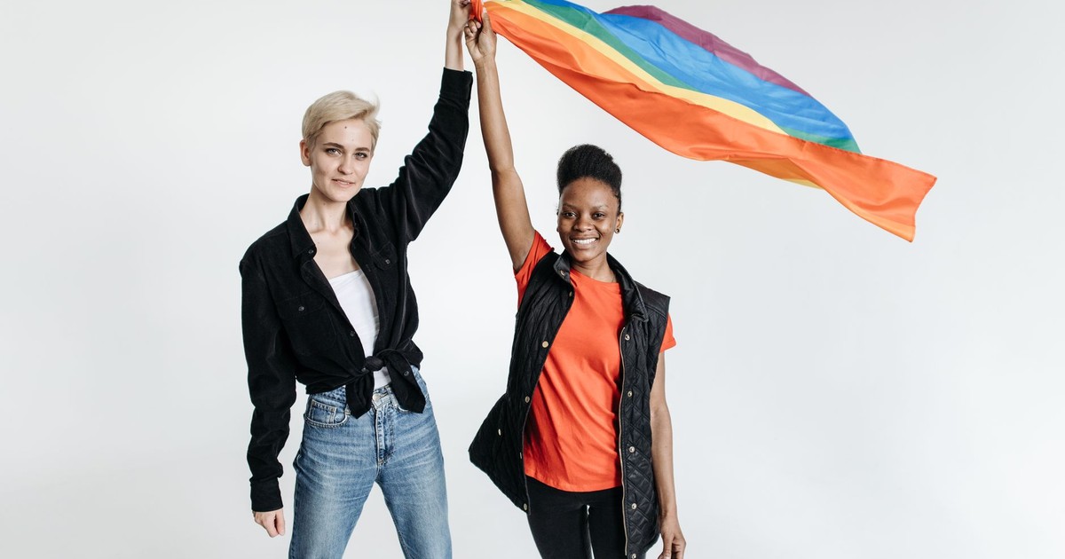 Two diverse women holding a rainbow flag on a white background, celebrating pride and inclusivity.