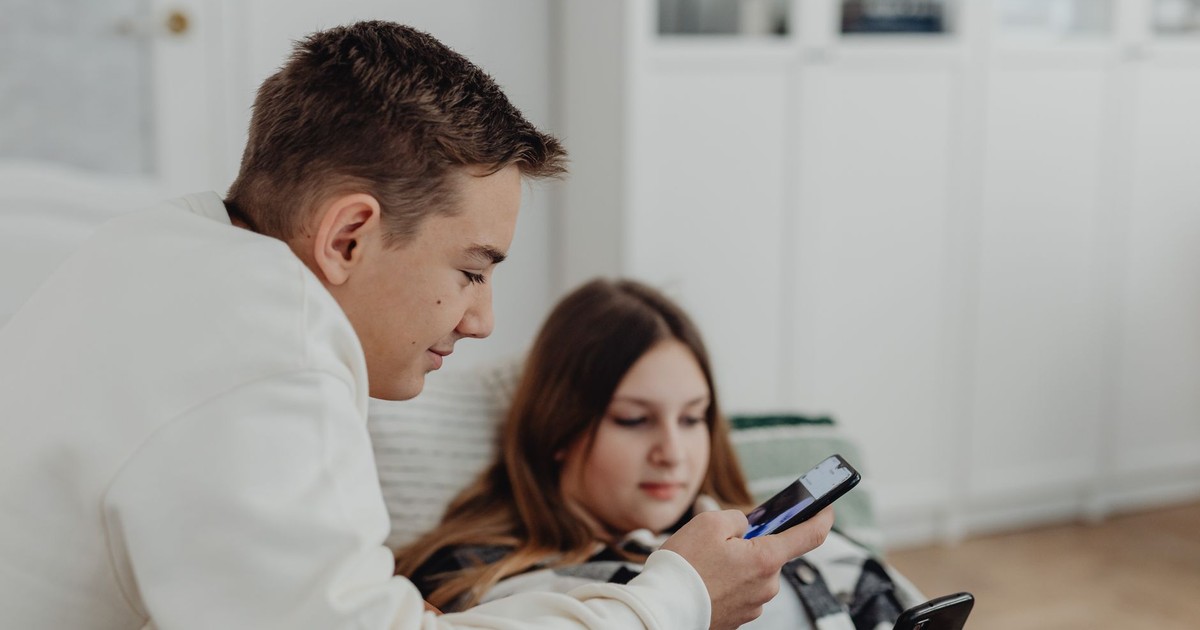 Two teenagers using smartphones in a cozy indoor setting, focused and relaxed.