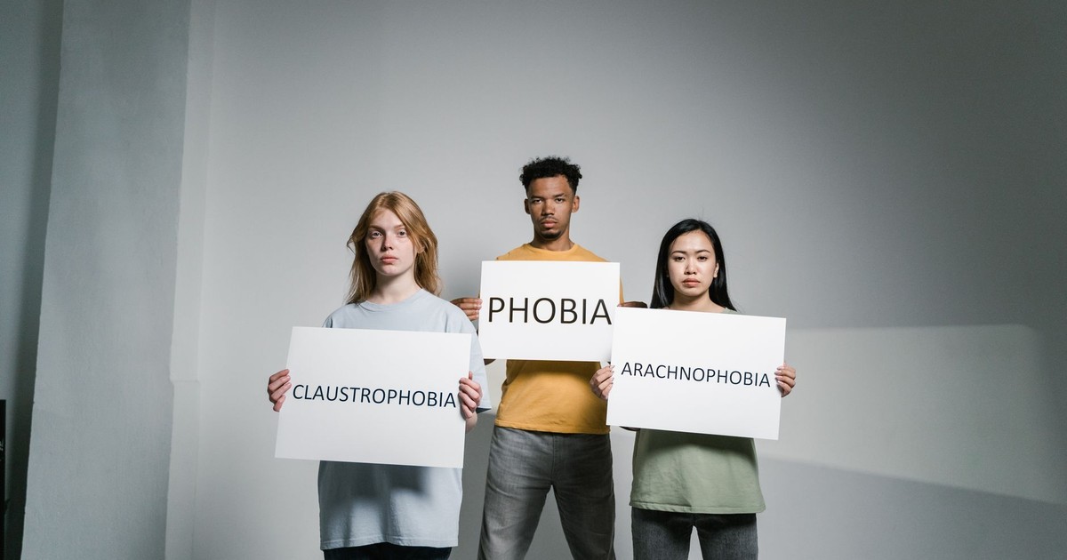 Three individuals holding signs representing various phobias, raising awareness.