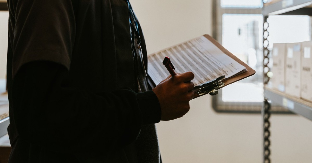 Industrial worker managing inventory in a warehouse with a clipboard and checklist.