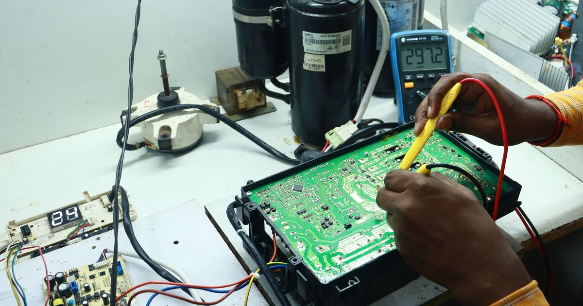 Technician working on AC PCB with tools and equipment, captured in New Delhi workshop.