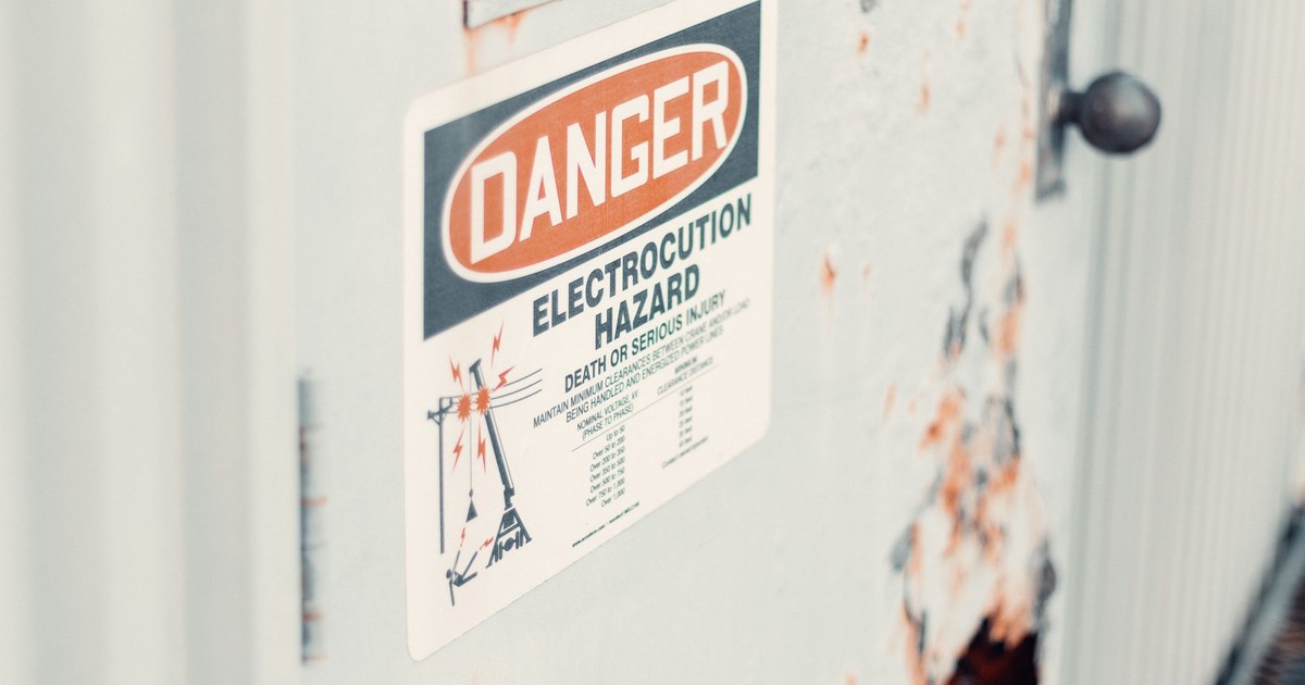 Close-up of a danger sign warning of electrocution hazard on a rusty utility door, indicating safety precautions.