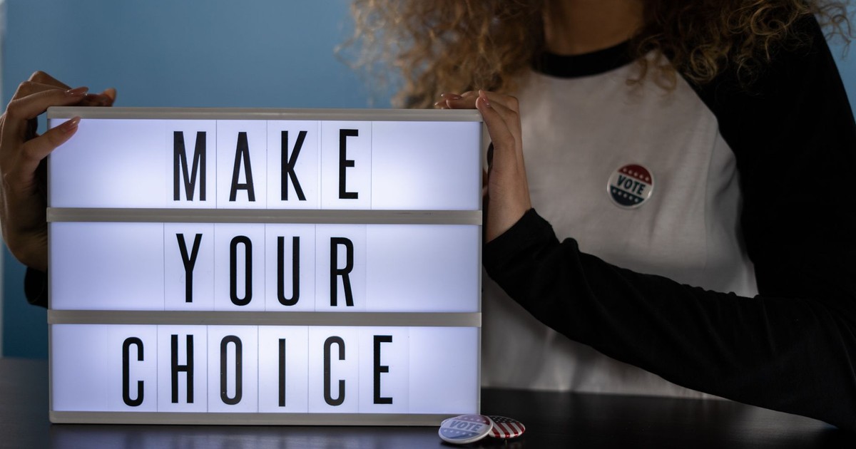 Woman holding lightbox with 'Make Your Choice' promoting civic duty and voting.