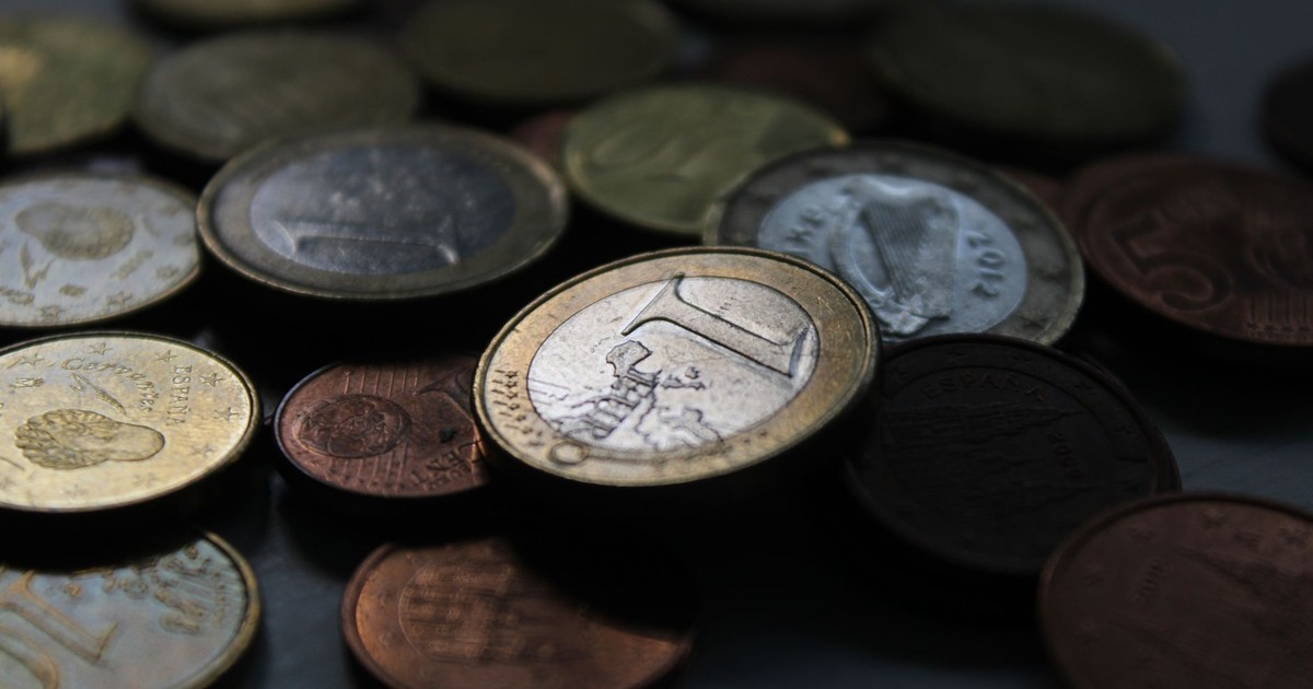 A close-up shot of Euro coins in various denominations scattered on a dark surface.