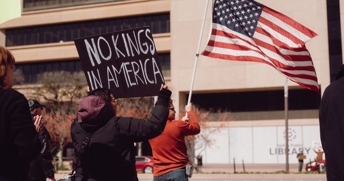 Demonstrators holding 'No Kings in America' sign and US flag in city protest.
