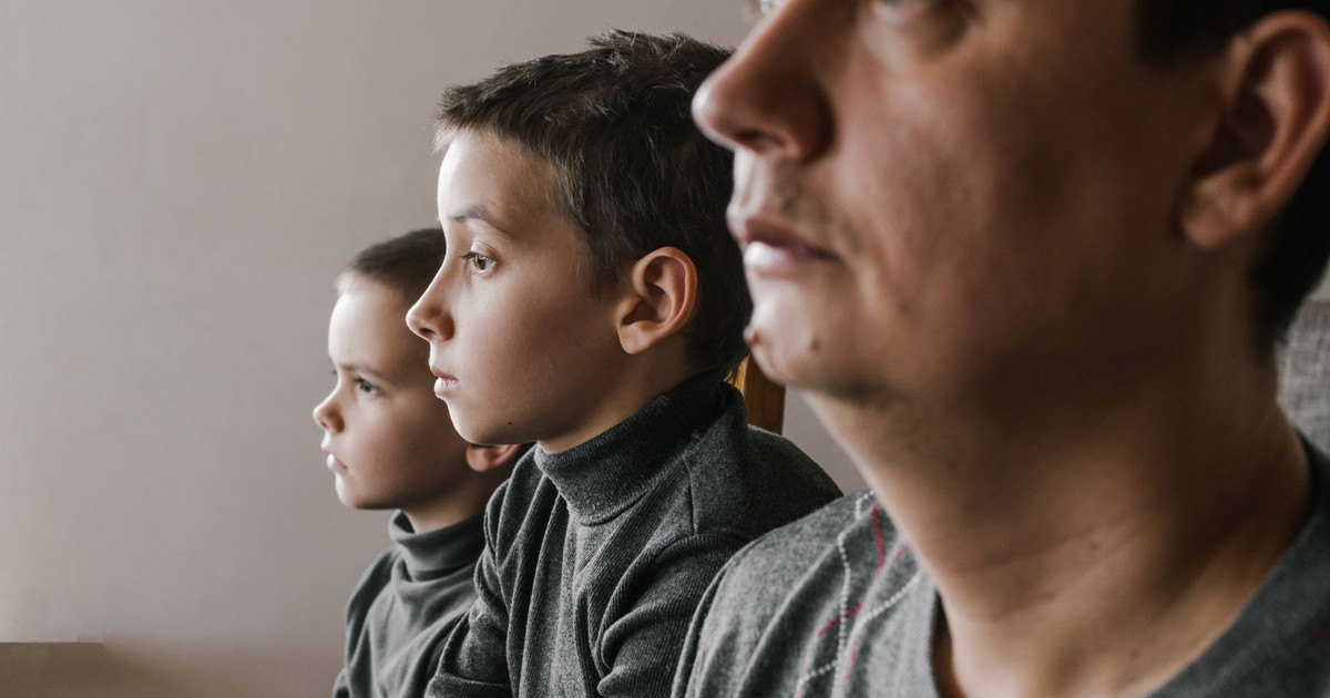 Side view of crop concentrated adult man sitting close to serious sons and looking away