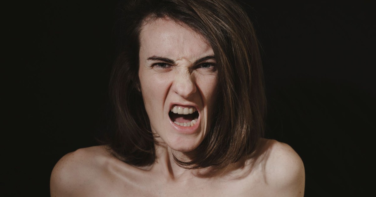 Close-up portrait of a woman expressing intense anger with an open mouth and bare shoulders.